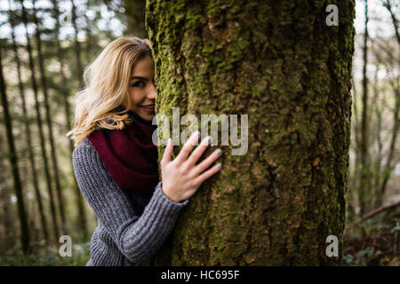 Beautiful woman hiding behind tree trunk in forest Stock Photo