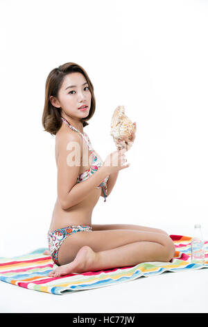 Woman in bikini with seashell sitting on beach towel Stock Photo