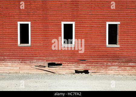 Three white window frames with no glass on a wall that is broken at the bottom. The wall belongs to a building in Kennicott, AK Stock Photo