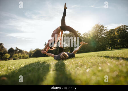 Outdoor shot of young man and woman doing yoga in pair. Couple doing acrobatic yoga exercise at park. Stock Photo