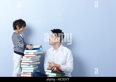 Side view of father and son with stacked books Stock Photo