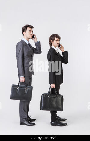 Businessman and woman disguising herself as businessman with briefcases standing talking on cellphones Stock Photo