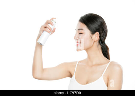 Side view portrait of young smiling woman spraying mist on her face Stock Photo
