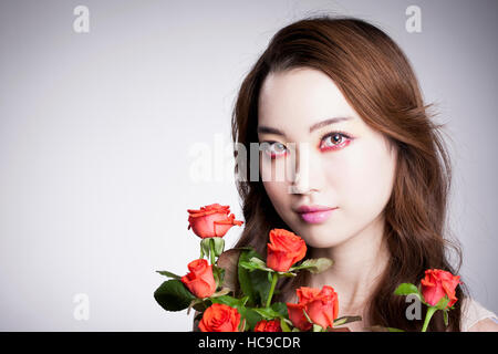 Portrait of young Korean woman in red eye liner posing with red roses Stock Photo