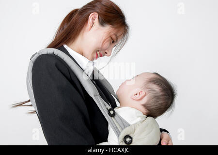 Side view portrait of smiling businesswoman hugging her baby in a carrier Stock Photo