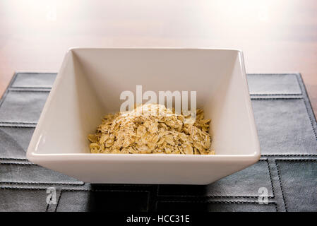 Bowl of dry porridge oats, on a black leather place mat. Stock Photo