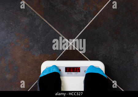 Bathroom scales on tiled floor with man wearing socks. Stock Photo