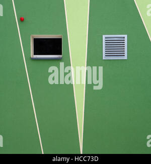 Fresh painted  rough green wall with two small windows and a red bulb of  security alarm system. Stock Photo