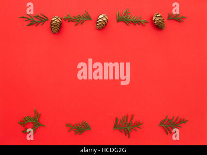 Christmas frame made of green thuja twigs and cones on red background. Top view, flat lay. Copy space for text Stock Photo