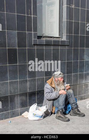 London, England, UK, 21 April 2016. A homeless man sitting underneath a window eating a sandwich. Stock Photo