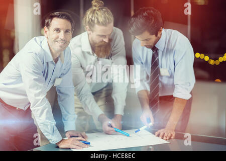 Businessman smiling while colleagues discussing over blueprint Stock Photo