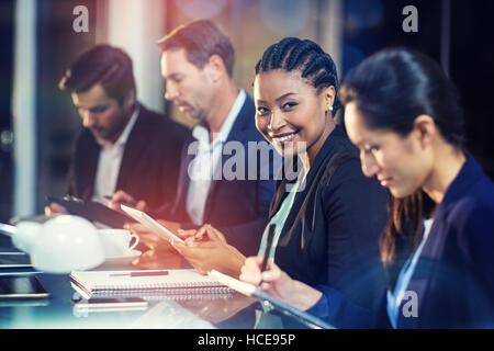 Businesswoman using digital tablet while colleagues writing notes Stock Photo