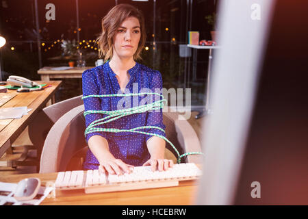 Businesswoman tied with rope while working at desk Stock Photo
