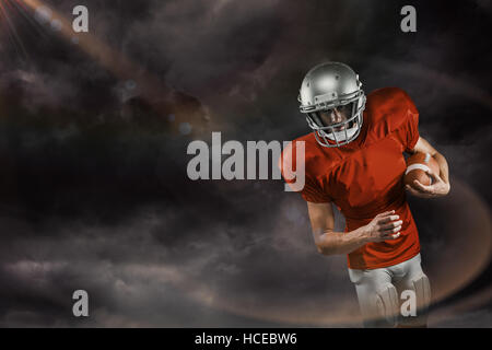 Composite image of american football player in red jersey looking down while holding ball Stock Photo