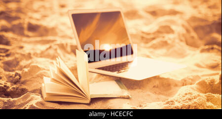 Composite image of open book and laptop on sand at beach Stock Photo