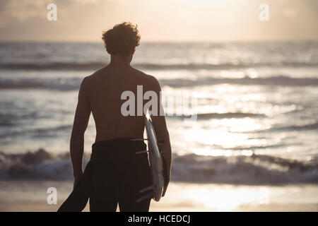 Man carrying surfboard standing on beach Stock Photo