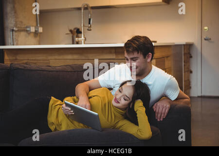 Cheerful couple lying together on sofa using digital tablet Stock Photo