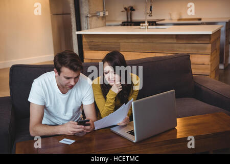Couple sitting on sofa discussing with financial documents in living room Stock Photo