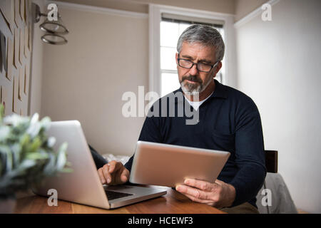 Man using laptop and digital tablet in living room Stock Photo