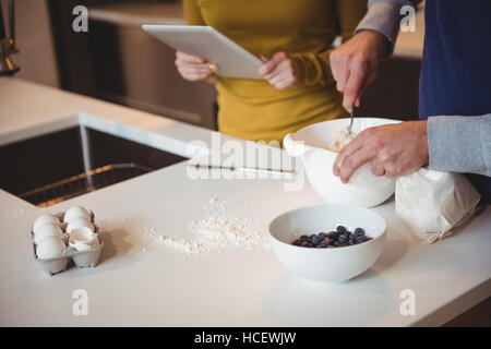 Couple using digital tablet while preparing cookies in kitchen Stock Photo