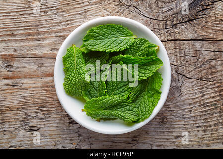 Bowl of mint leaves on wooden background, top view Stock Photo