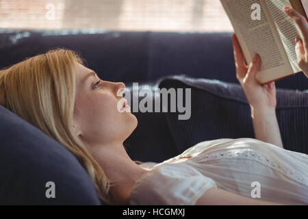 Beautiful woman lying on sofa and reading book in living room Stock Photo