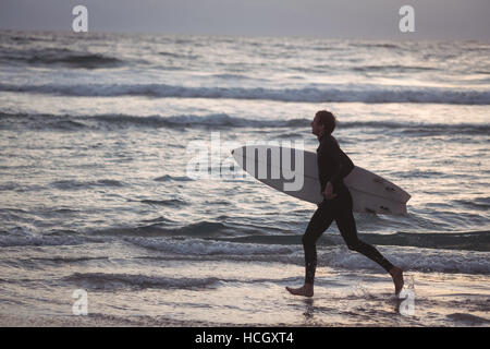 Man carrying surfboard running on beach Stock Photo