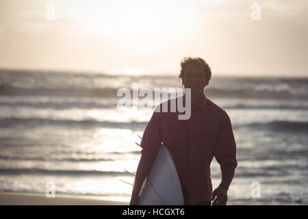 Man carrying surfboard standing on beach Stock Photo