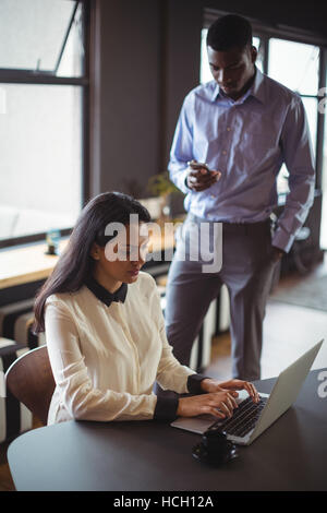 Businesswoman working on laptop while man using mobile phone Stock Photo