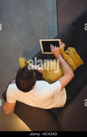 Cheerful couple lying together on sofa using digital tablet Stock Photo