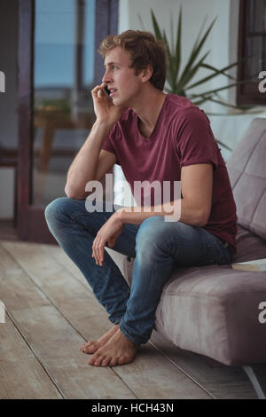 Man sitting on sofa and talking on mobile phone Stock Photo