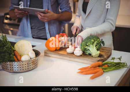 Mid section of couple using digital tablet while chopping vegetables Stock Photo