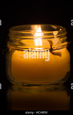 Beeswax candle (lit) in a glass jar on a black background with a reflection, longer exposure Stock Photo