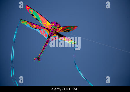 Colorful dragonfly kite with blue tails and a string flying in a blue sky Stock Photo