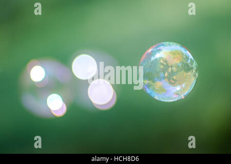 One bright soap bubble floating in focus with two de-focused bubbles behind it, with reflection of trees, grass, and sky, on a green background Stock Photo