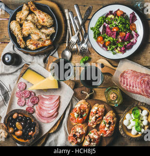 Home dinner, party table arrangement. Rustic table set with salad, olives, chicken, tomato, feta cheese brushettas, snacks and red wine, top view. Slo Stock Photo