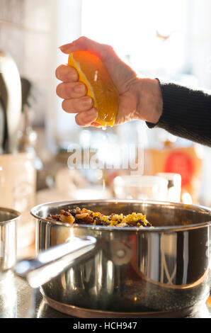 Woman squeezing fresh orange juice in to a saucepan of mixed fruit. Stock Photo