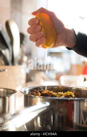 Woman squeezing fresh orange juice in to a saucepan of mixed fruit. Stock Photo