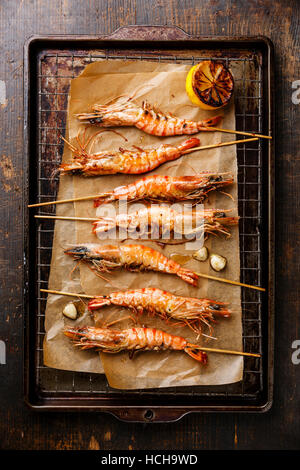 Grilled fried Tiger prawns shrimps on skewers and lemon on metal grid baking sheet background Stock Photo