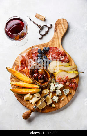 Meat and cheese plate antipasti snack with Prosciutto ham, Parmesan, Blue cheese, Cantaloupe melon and Olives on olive wood serving board on concrete Stock Photo