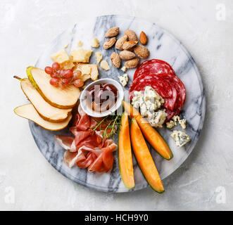 Meat and cheese plate antipasti snack with Prosciutto ham, Salami, Parmesan, Blue cheese, Cantaloupe melon and Olives on marble board Stock Photo