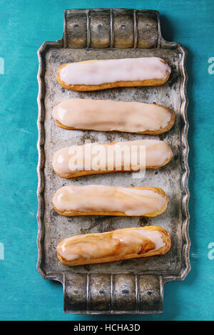 Homemade Coffee eclairs with different glaze on vintage metal tray over turquoise wood background with copy space. Top view. Stock Photo