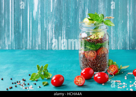 Salad with quinoa, spinach, tomatoes and zucchini in glass mason jars, standing with fresh vegetables over bright turquoise wooden background. Healthy Stock Photo