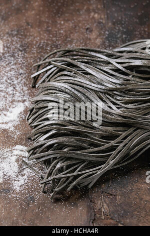 Raw uncooked black cuttlefish ink spaghetti pasta with flour over dark wooden background. Top view with space for text. Stock Photo