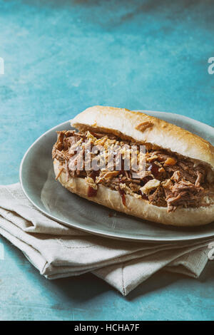 Variety of pulled pork sandwiches with meat, fried onion and bbq ketchup, served on gray plate and textile napkin over bright blue wooden background. Stock Photo