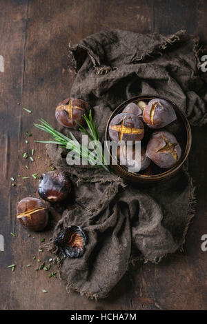 Roasted chestnuts in the ashes with rosemary in tin can on sackcloth over old dark wooden background. Top view with space for text. Stock Photo