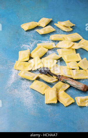 Fresh maked raw uncooked italian pasta ravioli with flour and vintage pasta cutter over bright blue wooden background. Top view with copy space. Stock Photo