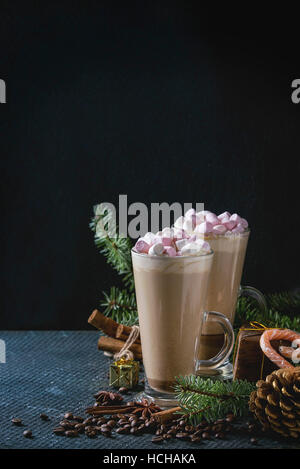 Two glasses of cafe latte with pink marshmallow with Christmas decor, candies, spices, coffee beans and fir tree over dark texture background. Top vie Stock Photo