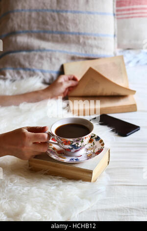 Female sitting on the bed,leafing through a book and drinking a cup of coffee. Stock Photo