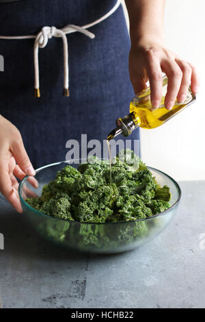 Female pouring olive oil over fresh kale leaves cabbage in a bowl Stock Photo